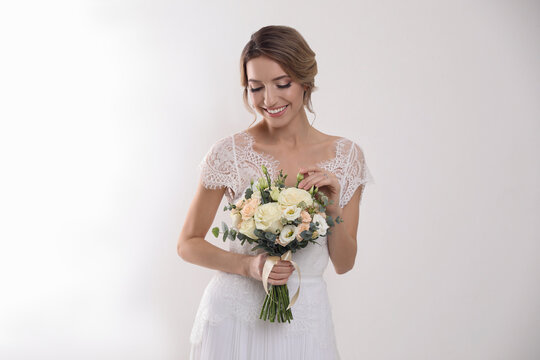 Young bride with elegant hairstyle holding wedding bouquet on white background