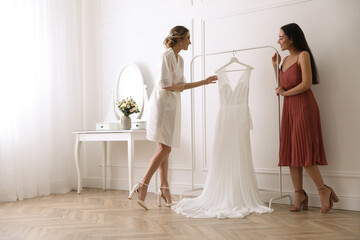 Naklejka premium Young bride with her friend near wedding dress indoors