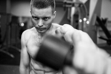 sculpted muscular guy trains his deltoids doing dumbbell swings in front of him