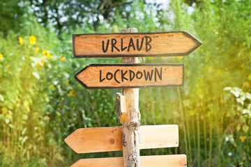 Wooden direction sign with the German word Urlaub (vacation) and Lockdown