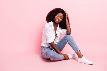 Full size photo of nice optimistic lady sit look empty space wear shirt jeans isolated on pastel pink color background