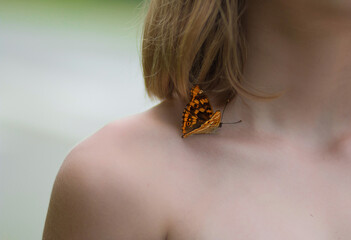 A butterfly sits on the naked shoulder of a young girl. 