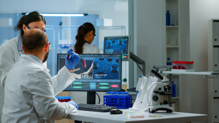 Group of scientists working in modern equipped laboratory pointing on computer desktop. Team of doctors examining vaccine evolution using high tech researching diagnosis against covid19 virus