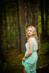 Young beautiful blonde in a light green dress posing in the woods in summer, selective focus