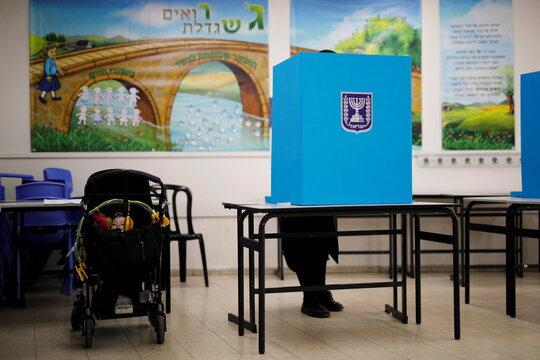 A baby sits in a stroller while an ultra-Orthodox Jewish man stands behind a voting booth as he votes in Israel's general election at a polling station in Ashdod
