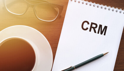 CRM Customer Relationship Marketing - text on paper with cup of coffee and glasses on wooden background in sinlight.