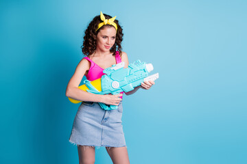 Photo of serious charming woman look empty space wear pink singlet hold water gun isolated on blue color background