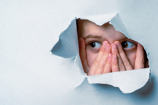 Portrait of young cute scared child girl with wide open eyes looking outside through a hole in the wall. Copy space for text.