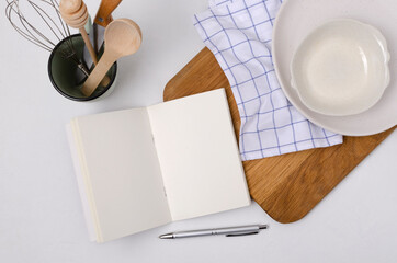 Top view of recipes book, wooden board, plates, utensils on the white kitchen table.Empty space