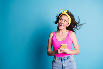 Photo of young cheerful girl happy smile dream look empty space hold cellphone isolated over blue color background