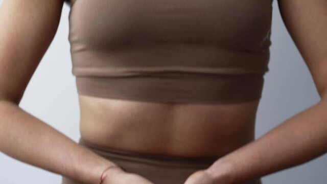 Attractive sportive young woman in stylish beige tracksuit does mudra practicing yoga in lotus pose on floor in light room extreme close view