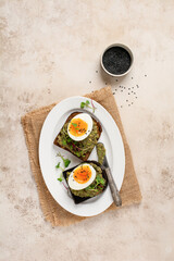 Healthy sandwich with avocado, eggs and microgreens on toast on a serving plate for breakfast. Healthy nutrition dietary concept. Top view