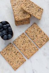 Some healthy piled crackers and some others in a diagonal row next to a tray full of blueberries...
