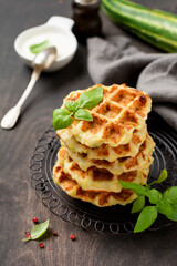 Homemade zucchini waffles stack with cheese, sause and leaf basil on old wooden dark background. Concept of keto diet food. Selective focus