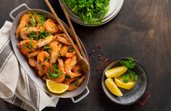 Roasted shrimps with garlic, lemon and parsley, black background, top view, copy space