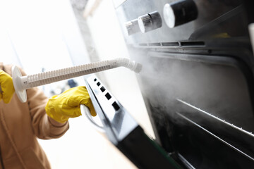 Woman in protective gloves washing oven with steam brush closeup