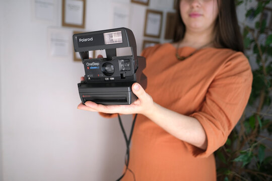 Frankfurt, Germany - March 2021: girl holding an old gadget for the production of instant photos in her hands, demonstrating Polaroid instantcamera of the 80s, a concept of retro technologies