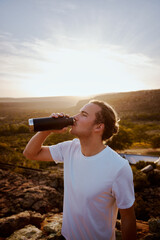 Portrait of young male runner drinking water during break after long run on mountain