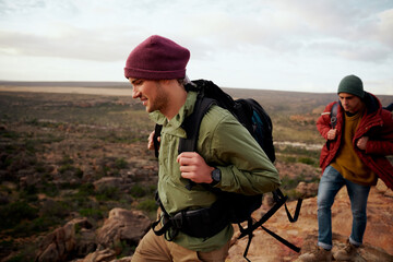 Two male friends with backpack and winter cap climbing mountain