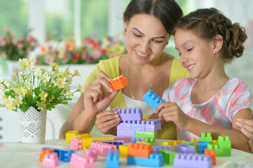  little daughter and mother playing with colorful plastic blocks at home