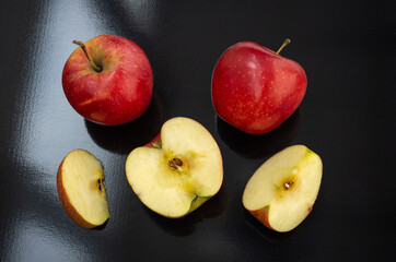 Two red apples with a half, a quarter and a slice isolated on a dark background. Top view.