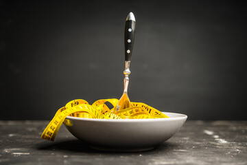 Yellow measuring tape in bowl like spaghetti with fork. Concept of diet. Selective focus. 