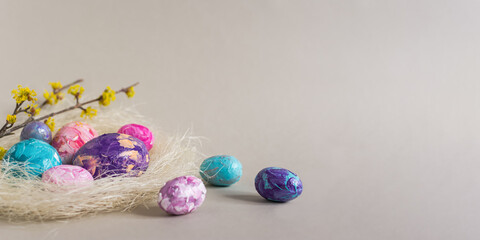 Easter painted eggs still life aesthetics. Festive Easter banner. Flat lay of the nest, blue, pink, purple eggs, flowering branches on a gray background. Happy Easter, greeting card. Copy space