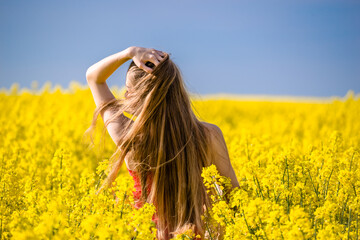 Naklejka na ściany i meble Happy woman in flowers of yellow blooming rapeseed. Spring portrait of young long hair girl. Concept of joy, happiness and freedom