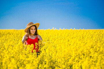 Fototapeta premium Summer portrait of girl in rapeseed. Rural scene with model woman enjoying sun and yellow blossom in field of canola. Concept of joy, happiness and freedom.