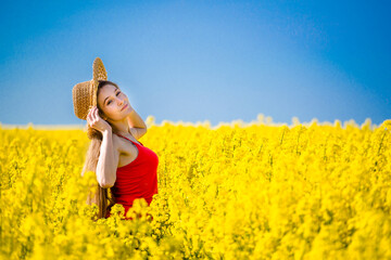 Fototapeta premium Summer portrait of woman in rapeseed. Rural scene with model girl enjoying sun in yellow flowers in field. Concept of joy, happiness and freedom.