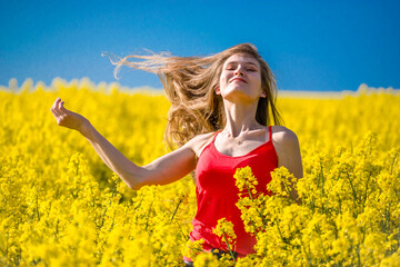 Happy woman in rapeseed field. Long hair, young smiling girl enjoying sun in blooming field. Freedom concept.