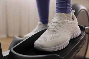 Woman using modern elliptical machine indoors, closeup