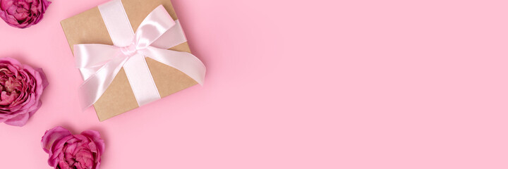 Banner with present with a tied ribbon and heads of rose flower on a pink background. Gentle composition with gift.
