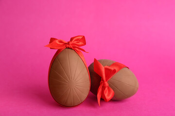 Sweet chocolate eggs with red bows on pink background