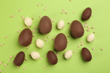 Sweet chocolate eggs on light green background, flat lay