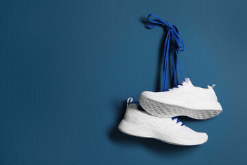 Pair of stylish shoes with laces hanging on blue wall, space for text