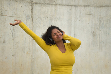 African american woman with afro hair and yellow t-shirt and bluetooth headphones dancing happily.