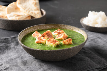Palak Paneer served with chapati and basmati rice on grey table. Indian vegetarian cuisine made of spinach and paneer cheese. Close up.