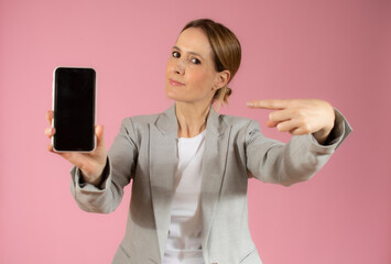 Portrait of a smiling young business woman showing blank screen mobile phone isolated over pink background