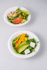 Two diet light salads with chicken, tomatoes, avocado, greens, white background. Healthy lunch. Take away food in eco paper plates. Concept restaurant delivery, environment protection.
