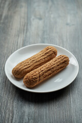 two eclairs with custard inside on a white plate. the plate stands on a gray wooden table. view from above