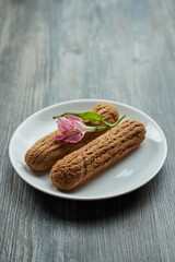 two delicious eclairs with cream are on a plate. on top of them lies a delicate flower