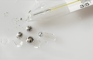Broken glass mercury thermometer on light grey surface. Mercury drops with glass fragments. Mercury...