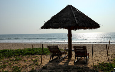 A Mesmerizing scene of a beach in twilight with Silhouetted thatched Umbrella made in Palm leaves and relaxing chairs in Karnataka,India.
