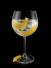 Cocktail gin tonic with lemon peels in a glass on black background