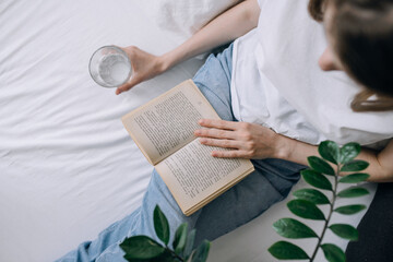 A young woman in casual clothes spends time reading a book and holding a glass of water top view