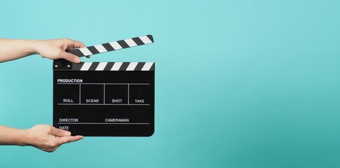 Naklejka premium Hand is holding Black clapper board or movie slate on green or mint or Tiffany Blue background.