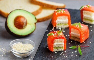 Mini sandwiches with smoked (salted) salmon or trout, avocado, cream cheese, sesame seeds and micro-greens on white bread. A delicious snack. Canapes. Tapas. Breakfast. Selective Focus