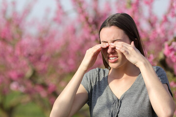 Woman scratching itchy eyes in spring in a flowers field