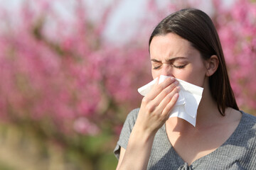 Woman blowing on tissue suffering allergy in spring in a field